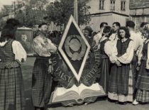 The members of Kaunas University folk ensemble are preparing for participation in the May 1st parade, 1950. Student R. Tamutis, who became the leader of the dance group in 1951, is standing next to the stylised sign.